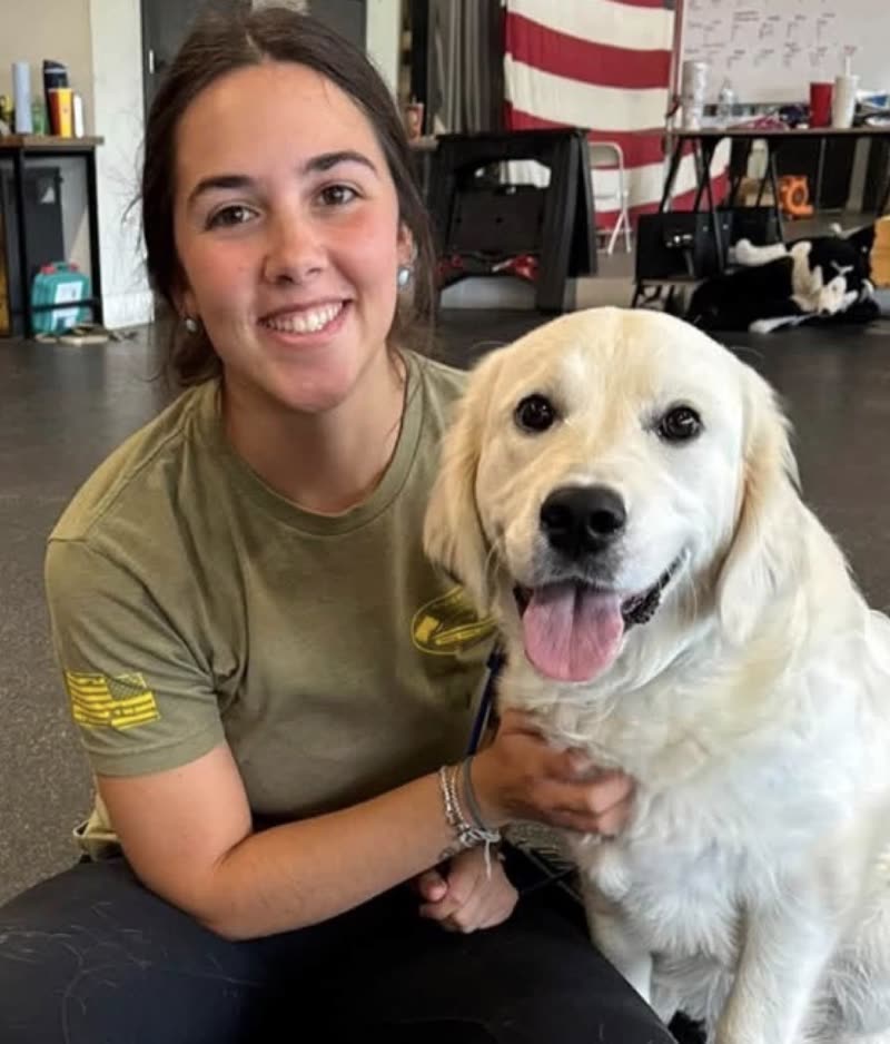 A trainer kneeling with her arm around a cream golden retriever inside the Ridgeside K9 Winchester training facility